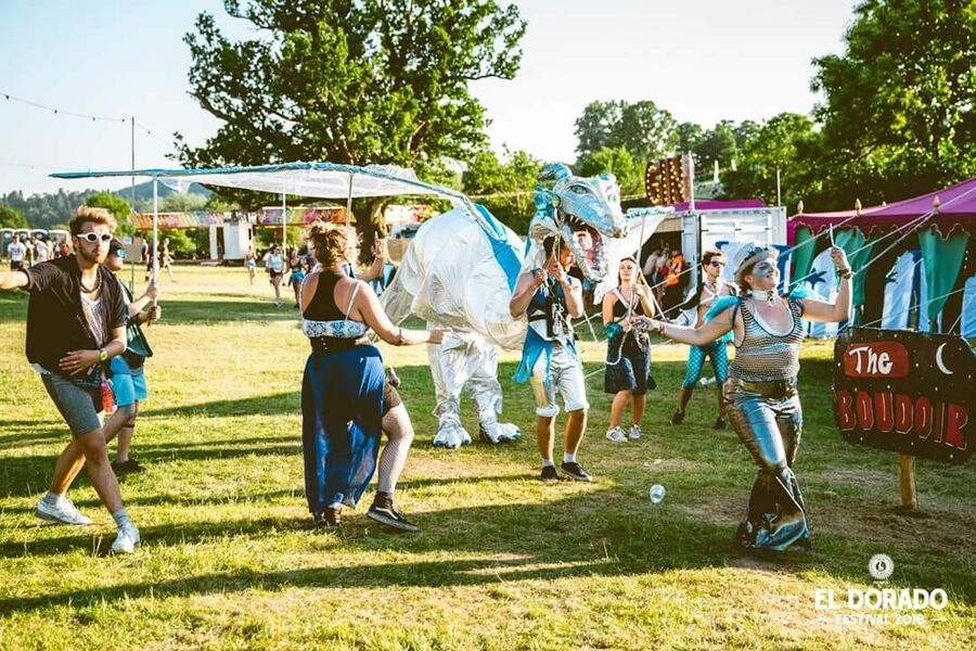 A pale dragon puppet carried across a festival field by performers in blue and silver.