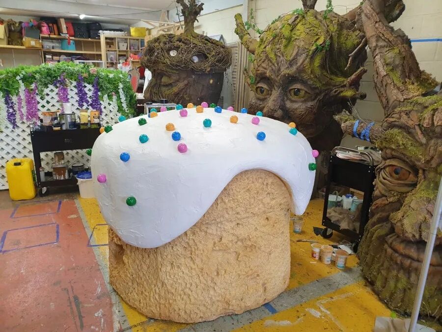 A workshop holding a giant iced cupcake prop and several carved tree-face sculptures.