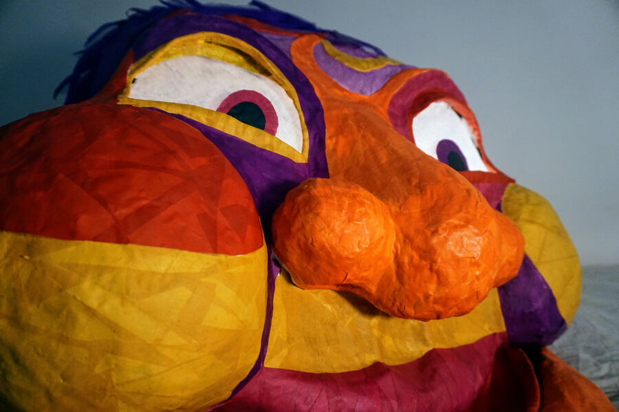 A large papier-mache monster head in yellow, orange and purple, with a bulbous nose.