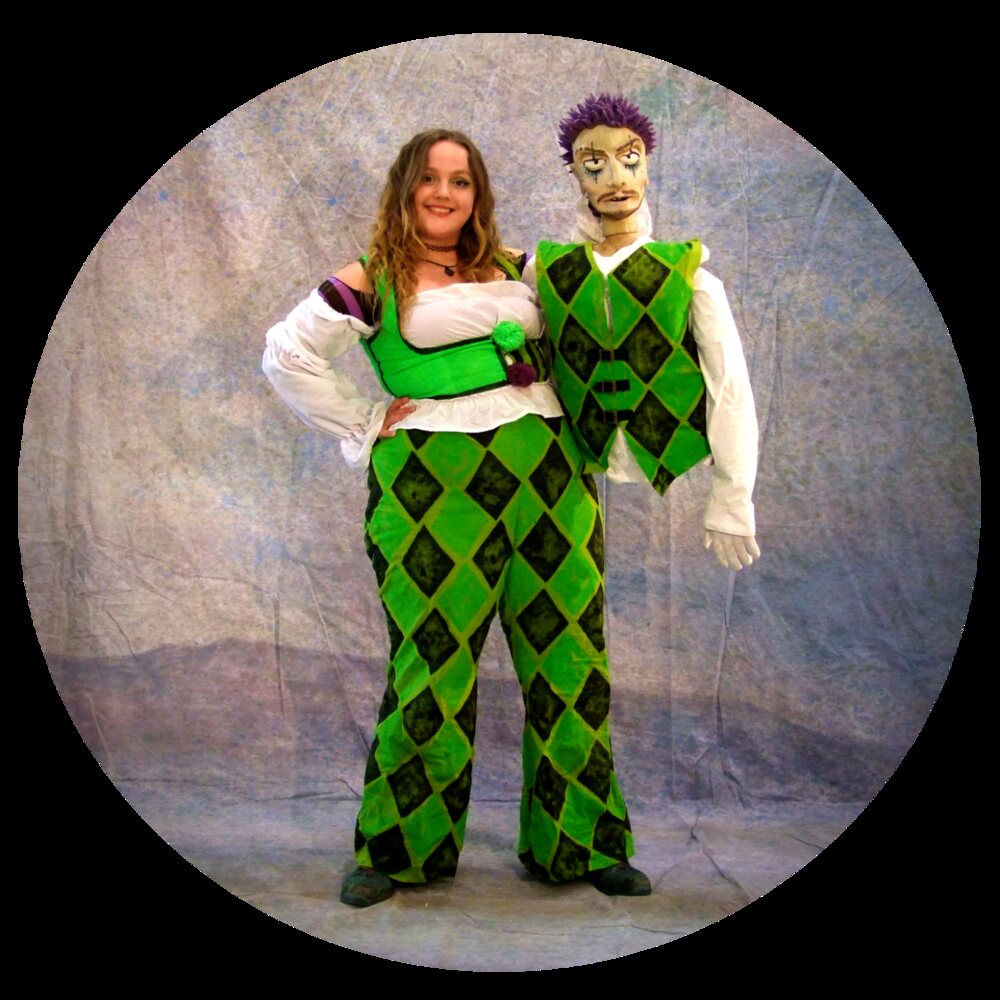 Rhianna Yates in a green harlequin costume, standing beside a life-size harlequin puppet dressed to match.